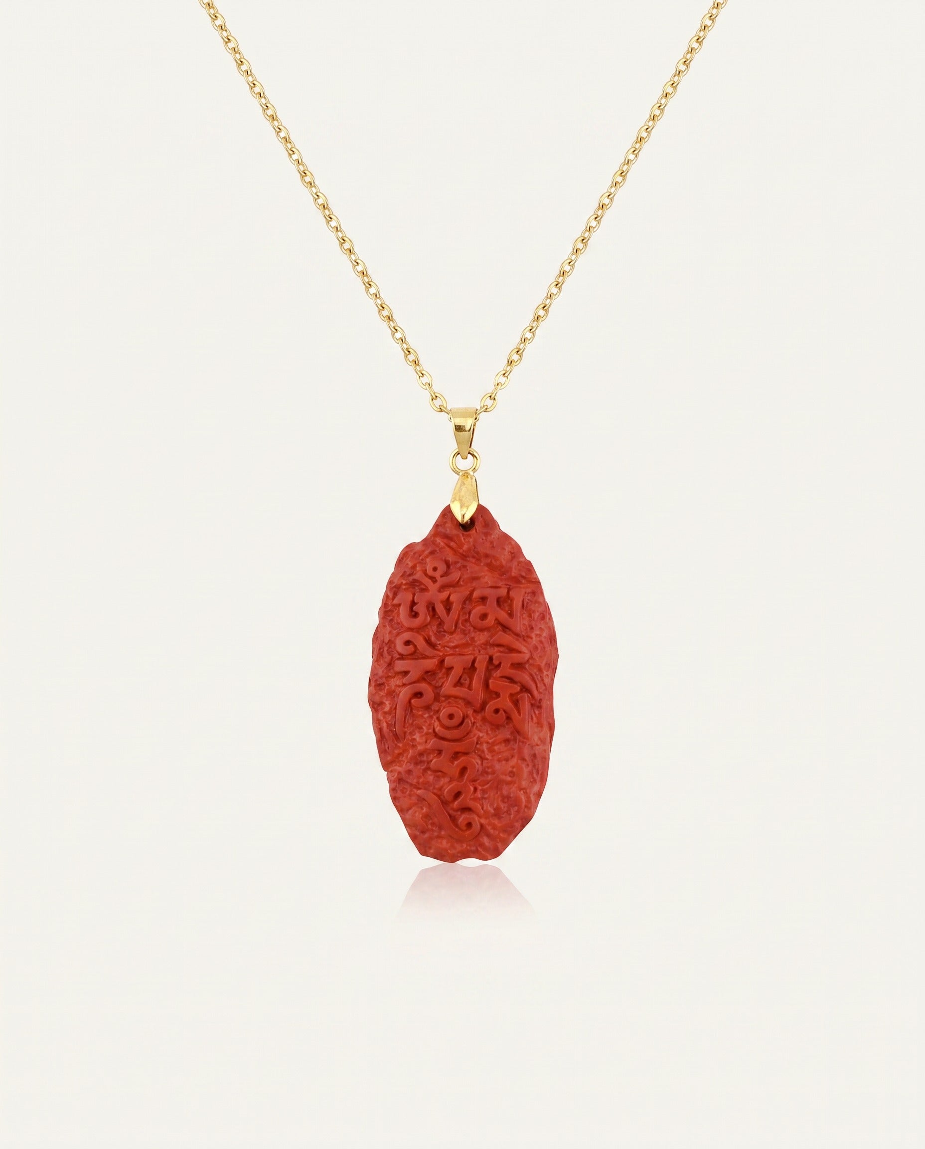Six Character Mantra cinnabar necklace on gold chain, ivory studio background