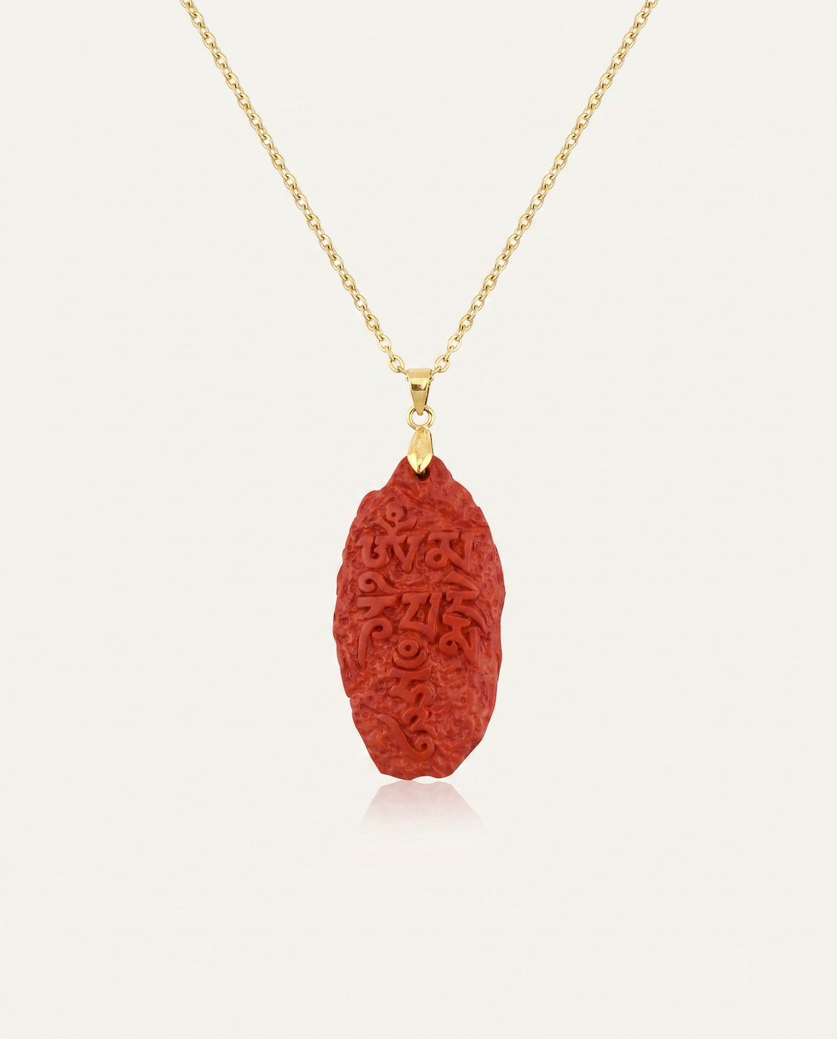 Six Character Mantra cinnabar necklace on gold chain, ivory studio background